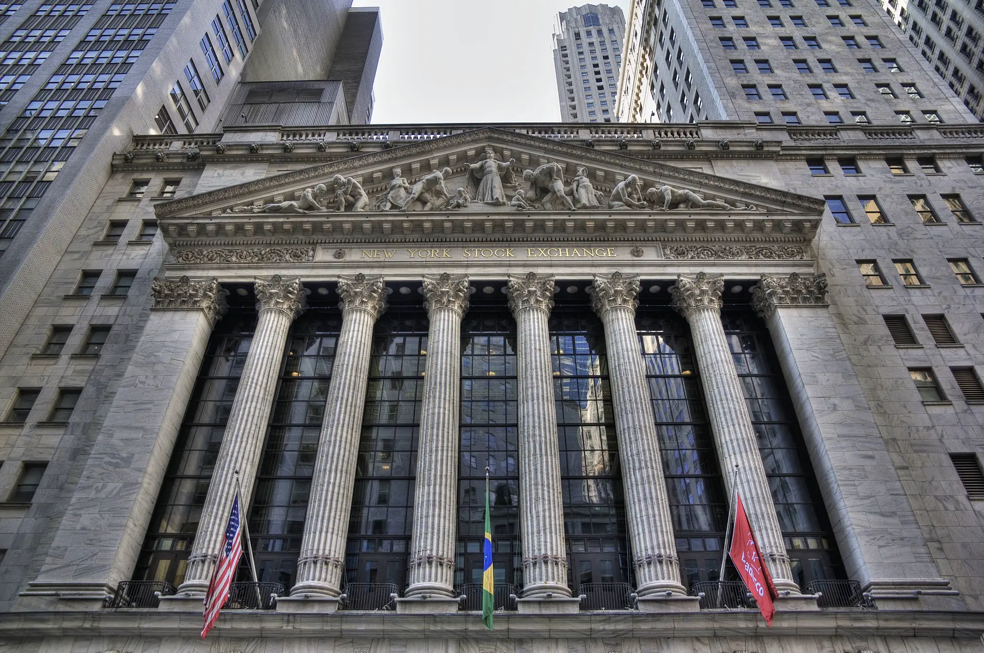 חזית בורסת ניו יורק (NYSE) המפורסמת - מבנה היסטורי בסגנון ניאו-קלאסי עם עמודי שיש מרשימים, פרונטון מעוטר ודגלים. מרכז הפיננסים העולמי בוול סטריט, מנהטן, המסמל את לב הכלכלה האמריקאית והעולמית ומקום מסחר מרכזי בשוקי ההון הבינלאומיים.